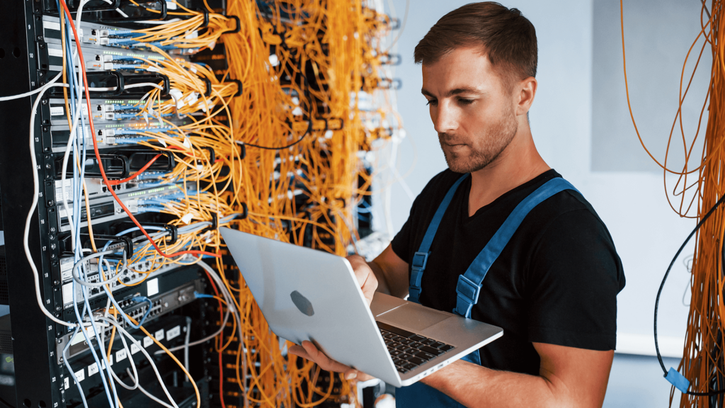man with a laptop looking at wires connected to server racks