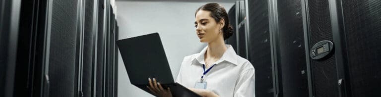 IT technician using a laptop by server racks
